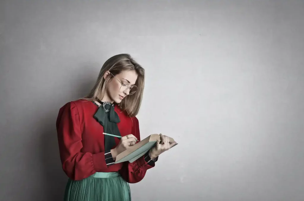 A woman wearing a red shirt and a green skirt taking notes.